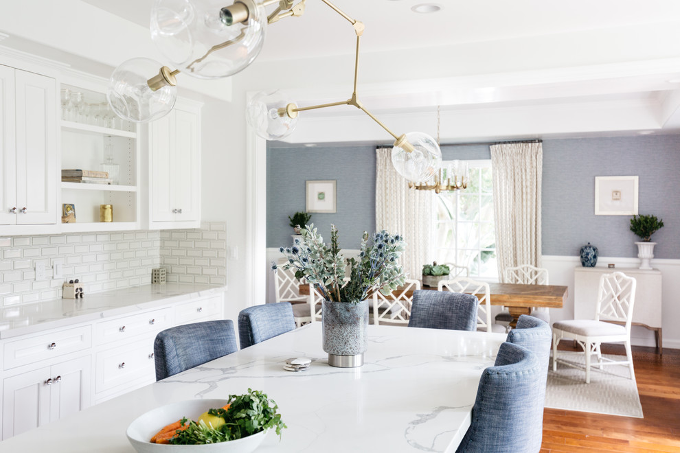 Inspiration for a mid-sized transitional u-shaped medium tone wood floor and brown floor eat-in kitchen remodel in Los Angeles with a farmhouse sink, recessed-panel cabinets, white cabinets, quartzite countertops, white backsplash, subway tile backsplash, stainless steel appliances, an island and white countertops