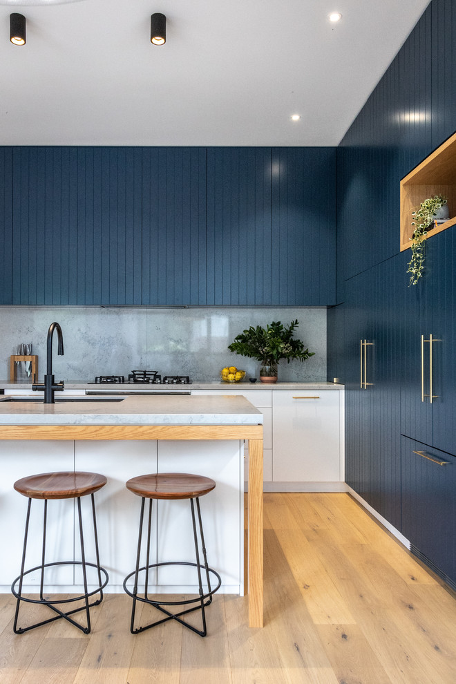 Photo of a contemporary galley kitchen in Sydney with an undermount sink, blue cabinets, marble benchtops, multi-coloured splashback, marble splashback, black appliances, light hardwood floors, with island and grey benchtop.