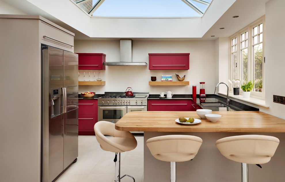 Design ideas for a mid-sized eclectic u-shaped kitchen in London with a double-bowl sink, flat-panel cabinets, red cabinets and stainless steel appliances.
