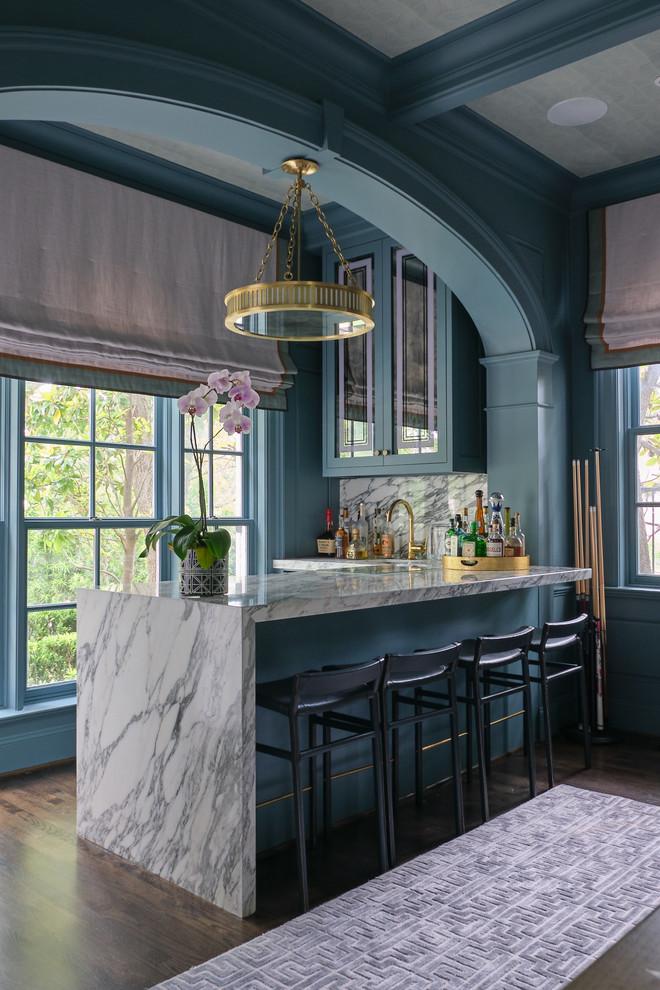 This is an example of a traditional l-shaped wet bar in Dallas with glass-front cabinets, blue cabinets, grey splashback, dark hardwood floors, brown floor and grey benchtop.