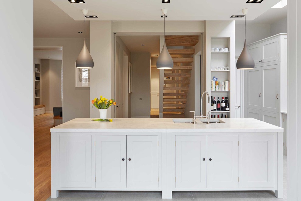 This is an example of a large modern l-shaped open plan kitchen in London with a double-bowl sink, shaker cabinets, white cabinets, marble benchtops, stone slab splashback, stainless steel appliances, marble floors and with island.