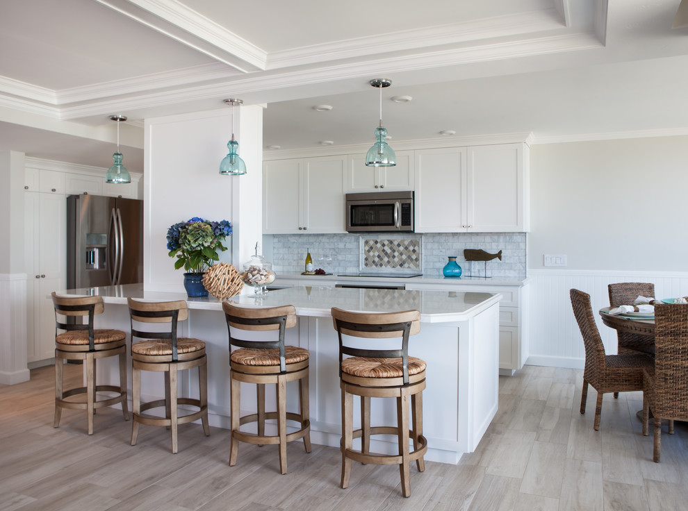 Photo of a mid-sized beach style l-shaped eat-in kitchen in San Diego with a double-bowl sink, beaded inset cabinets, white cabinets, solid surface benchtops, multi-coloured splashback, ceramic splashback, stainless steel appliances, porcelain floors and with island.