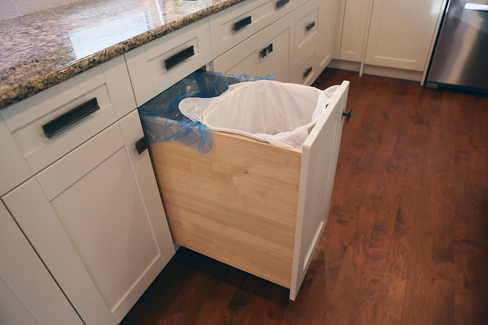 Example of a mid-sized transitional l-shaped medium tone wood floor and brown floor open concept kitchen design in Calgary with an undermount sink, shaker cabinets, white cabinets, granite countertops, white backsplash, mosaic tile backsplash, stainless steel appliances, an island and beige countertops