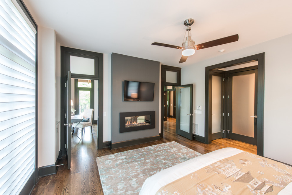 Huge transitional master medium tone wood floor bedroom photo with white walls, a ribbon fireplace and a plaster fireplace