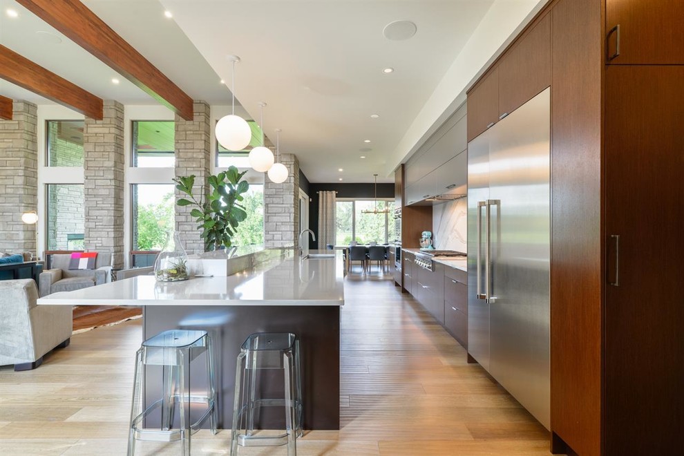 Trendy galley medium tone wood floor and brown floor kitchen photo in Edmonton with flat-panel cabinets, dark wood cabinets, white backsplash, stone slab backsplash, stainless steel appliances and an island