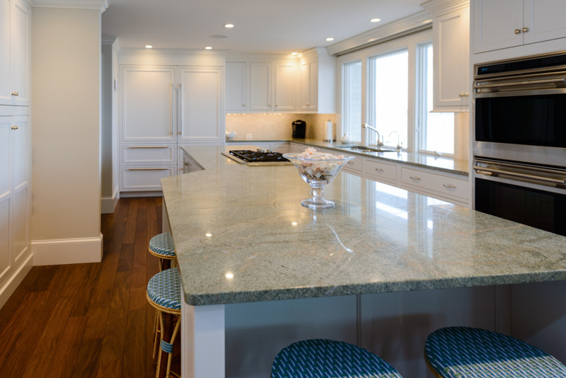 Inspiration for a transitional medium tone wood floor kitchen remodel in Boston with a triple-bowl sink, recessed-panel cabinets, white cabinets, granite countertops, white backsplash, mosaic tile backsplash, stainless steel appliances and an island