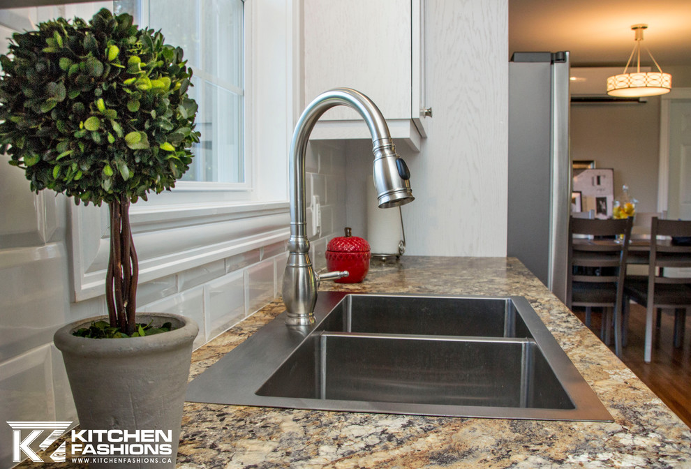 Mid-sized transitional l-shaped medium tone wood floor open concept kitchen photo with a drop-in sink, shaker cabinets, white cabinets, laminate countertops, white backsplash, subway tile backsplash, stainless steel appliances and an island