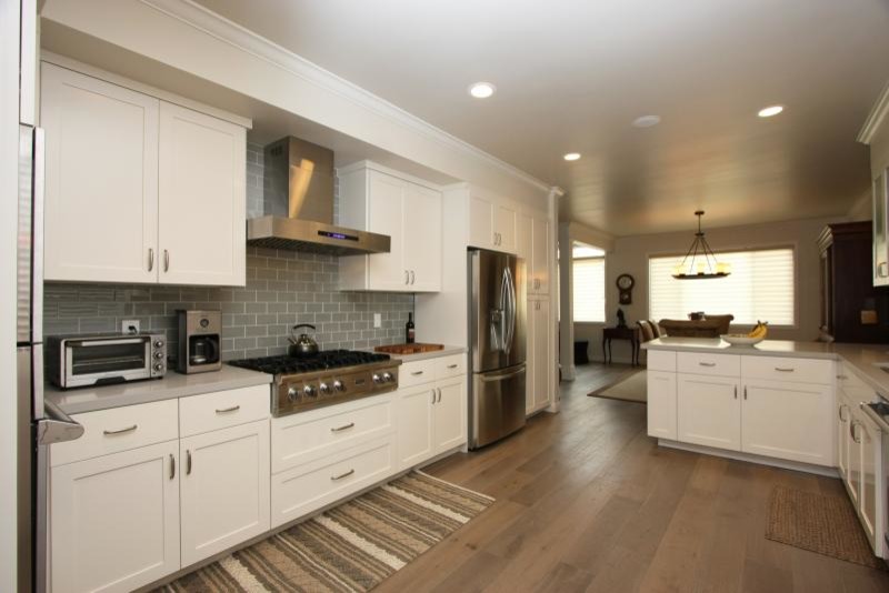 Inspiration for a large transitional l-shaped medium tone wood floor and brown floor eat-in kitchen remodel in Los Angeles with an undermount sink, shaker cabinets, white cabinets, soapstone countertops, metallic backsplash, subway tile backsplash, stainless steel appliances and a peninsula