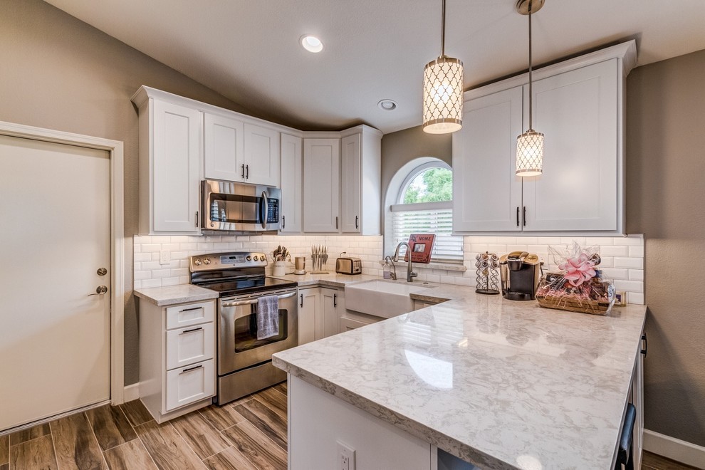 Example of a transitional u-shaped porcelain tile and beige floor eat-in kitchen design in Phoenix with a farmhouse sink, shaker cabinets, white cabinets, quartz countertops, white backsplash, subway tile backsplash, stainless steel appliances and white countertops