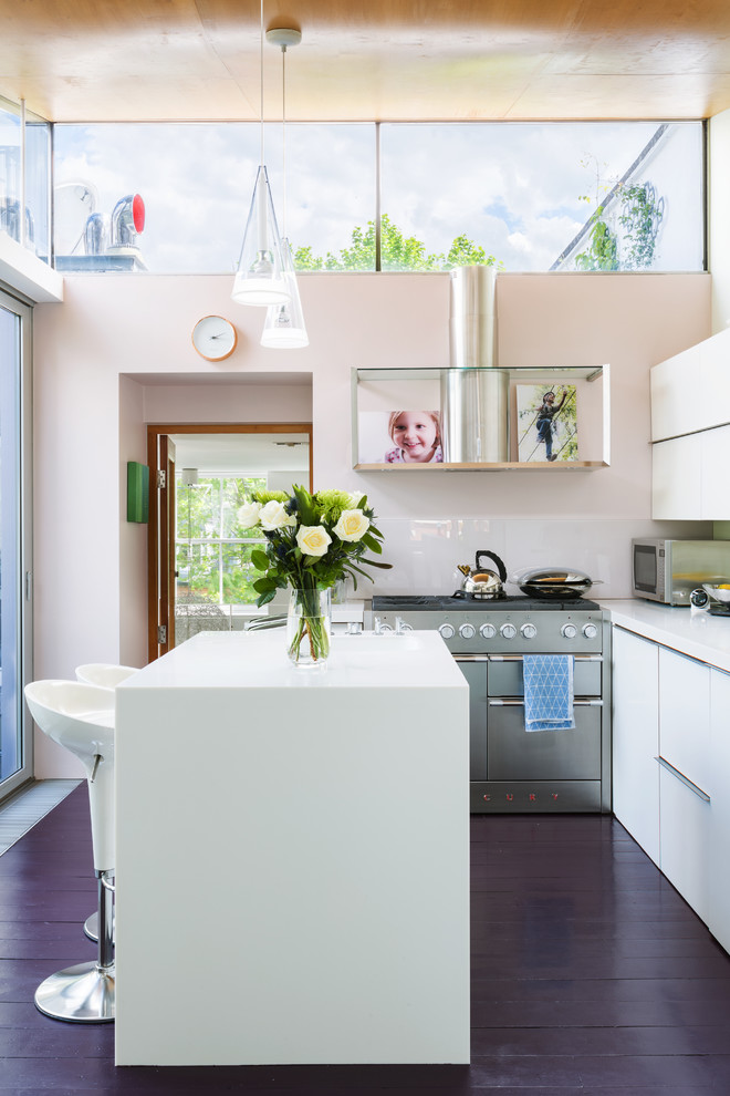 Design ideas for a mid-sized contemporary single-wall open plan kitchen in London with a drop-in sink, flat-panel cabinets, white cabinets, solid surface benchtops, glass sheet splashback, stainless steel appliances, painted wood floors and with island.