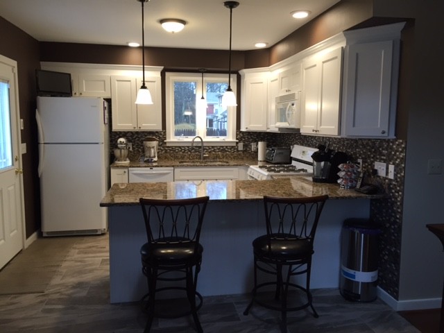 Eat-in kitchen - mid-sized transitional u-shaped porcelain tile eat-in kitchen idea in Boston with an undermount sink, recessed-panel cabinets, white cabinets, granite countertops, multicolored backsplash, mosaic tile backsplash, white appliances and a peninsula