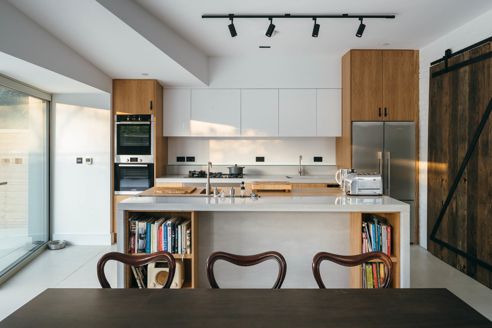 Design ideas for a transitional single-wall eat-in kitchen in London with an undermount sink, flat-panel cabinets, medium wood cabinets, stainless steel appliances, with island, beige floor and white benchtop.