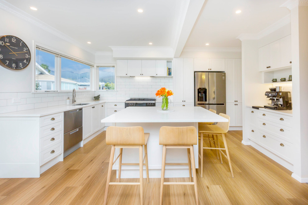 Inspiration for an expansive transitional u-shaped kitchen in Wellington with white cabinets, quartz benchtops, white splashback, subway tile splashback, stainless steel appliances, light hardwood floors, with island, white benchtop, a double-bowl sink, shaker cabinets and beige floor.