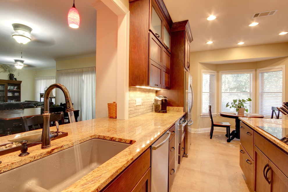 Inspiration for a transitional eat-in kitchen remodel in Miami with an undermount sink, shaker cabinets, brown cabinets, granite countertops, beige backsplash, stone tile backsplash and stainless steel appliances