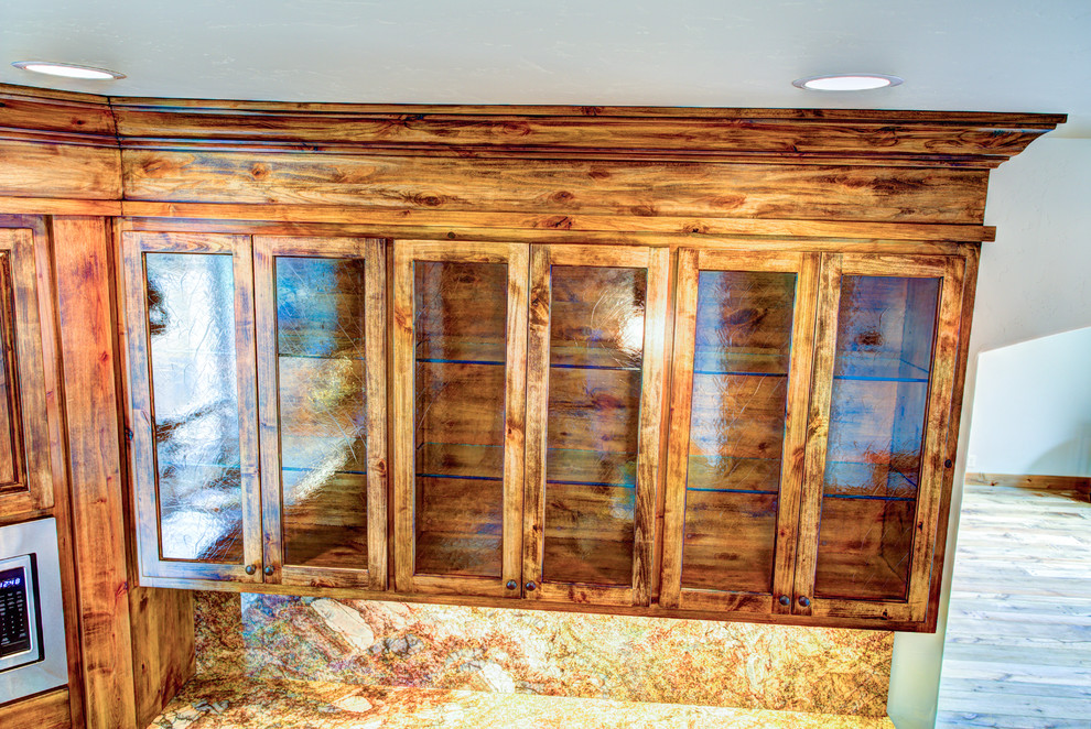 Example of a large mountain style u-shaped medium tone wood floor kitchen pantry design with a drop-in sink, glass-front cabinets, medium tone wood cabinets, beige backsplash, stainless steel appliances and an island