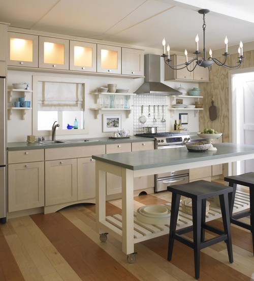 Slim mobile kitchen island on casters with slatted shelf and stone top, paired with light-wood kitchen cabinet and open shelves in a bright small kitchen.