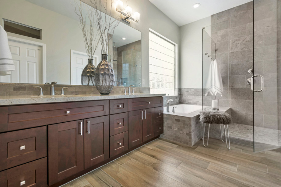 Inspiration for a large transitional master bathroom in Phoenix with raised-panel cabinets, brown cabinets, a drop-in tub, a corner shower, beige tile, porcelain tile, grey walls, porcelain floors, a drop-in sink, granite benchtops, brown floor and a hinged shower door.