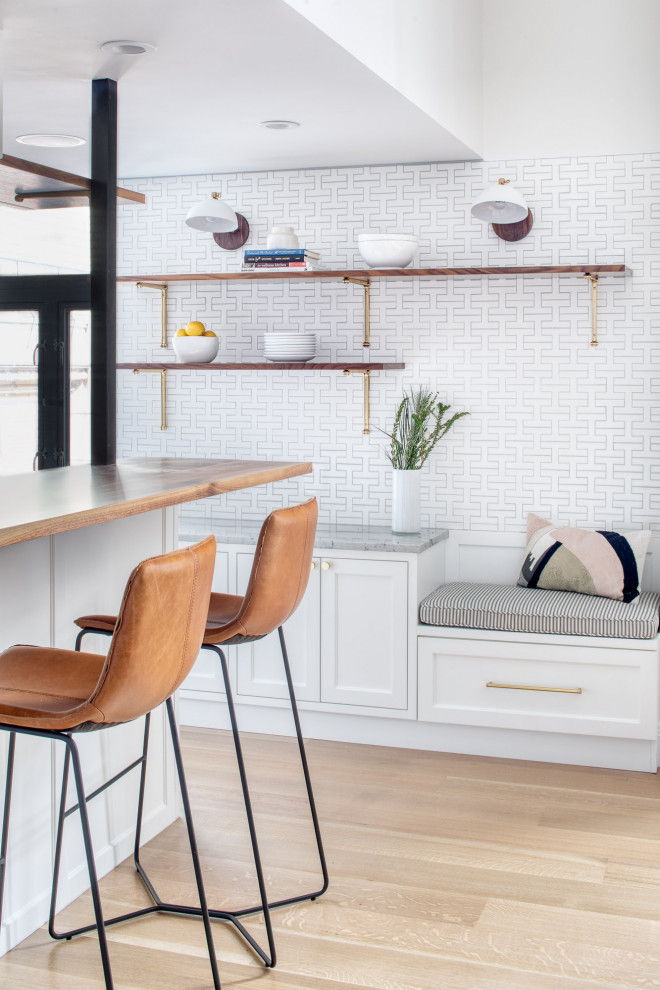 Mid-sized transitional galley light wood floor and brown floor eat-in kitchen photo in New York with a farmhouse sink, shaker cabinets, white cabinets, quartzite countertops, white backsplash, ceramic backsplash, stainless steel appliances, an island and gray countertops