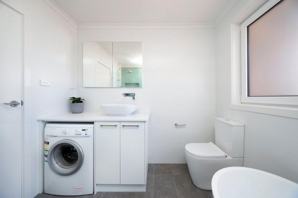 Inspiration for a mid-sized contemporary master bathroom in Canberra - Queanbeyan with flat-panel cabinets, white cabinets, a freestanding tub, a shower/bathtub combo, a one-piece toilet, green tile, ceramic tile, white walls, ceramic floors, a pedestal sink, laminate benchtops, grey floor, an open shower, white benchtops, a laundry, a single vanity and a freestanding vanity.