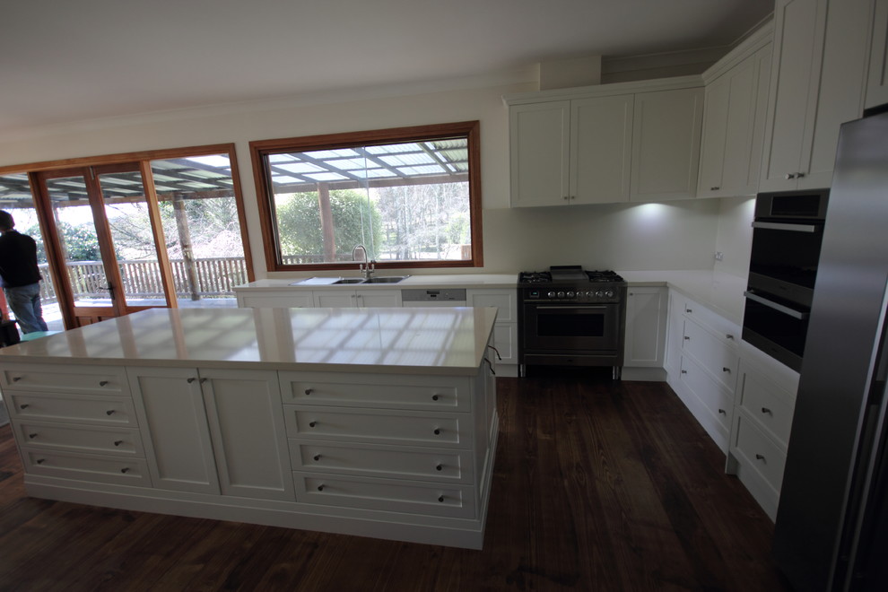 Photo of a large country l-shaped kitchen pantry in Sydney with a drop-in sink, shaker cabinets, white cabinets, beige splashback, glass sheet splashback, stainless steel appliances and with island.