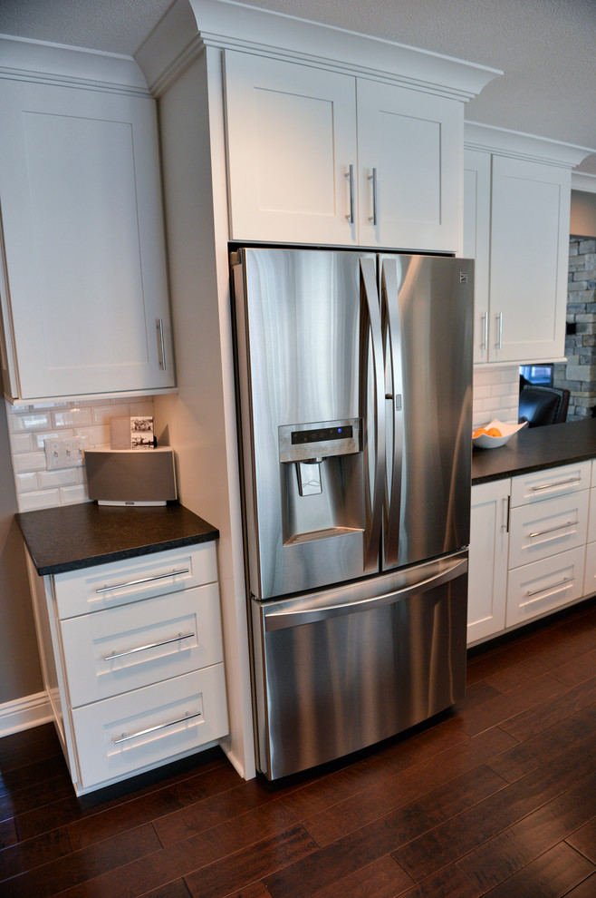 Inspiration for a transitional dark wood floor kitchen remodel in Cleveland with a drop-in sink, recessed-panel cabinets, white backsplash, ceramic backsplash, stainless steel appliances and an island
