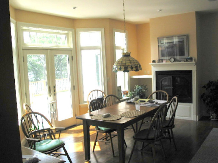 This is an example of a separate dining room in Portland Maine with yellow walls, light hardwood floors, a standard fireplace and a wood fireplace surround.