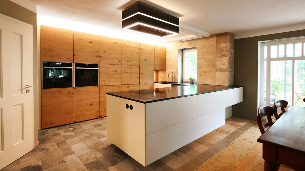 This is an example of a large contemporary u-shaped open plan kitchen in Munich with flat-panel cabinets, black appliances, with island, beige floor, beige cabinets and granite benchtops.