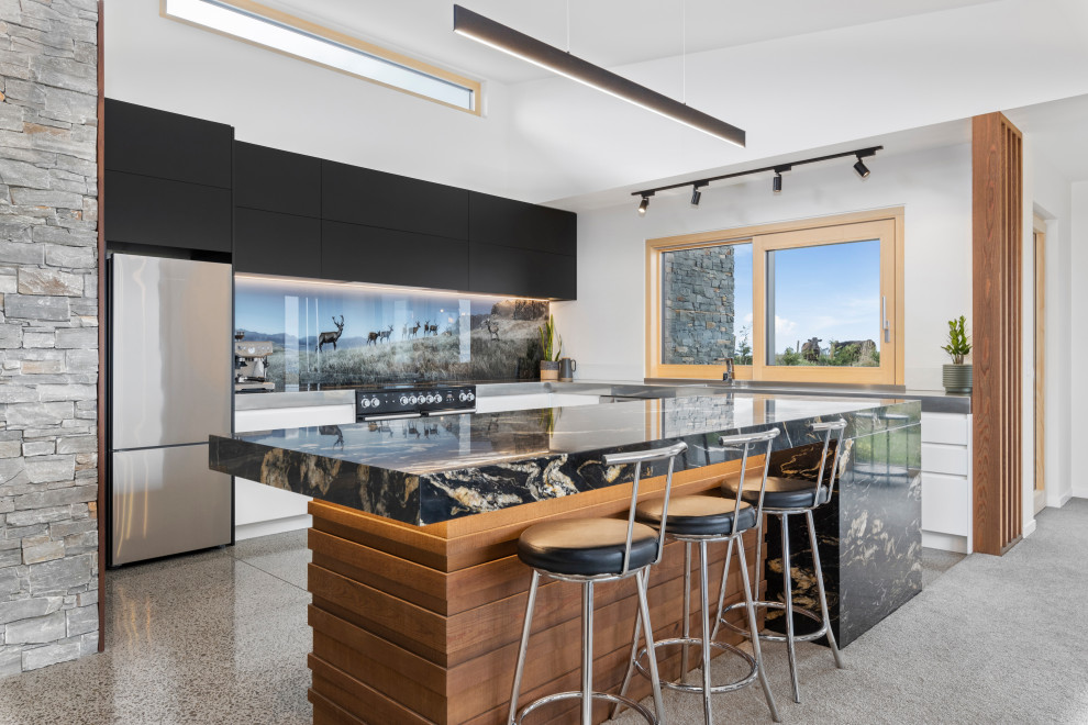 This is an example of a large rustic galley kitchen/diner in Other with a built-in sink, flat-panel cabinets, black cabinets, granite worktops, multi-coloured splashback, glass sheet splashback, black appliances, concrete flooring, an island, grey floors, black worktops and a vaulted ceiling.