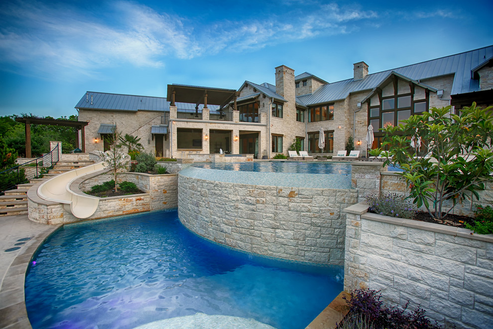 Design ideas for an expansive transitional backyard custom-shaped infinity pool in Dallas with a water slide and natural stone pavers.