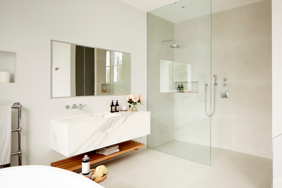 This is an example of a contemporary bathroom in London with a freestanding tub, a curbless shower, beige tile, white walls, a trough sink and an open shower.