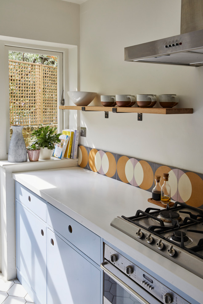 Small modern galley eat-in kitchen in London with flat-panel cabinets, blue cabinets, solid surface benchtops, yellow splashback, cement tile splashback, panelled appliances, ceramic floors, white floor and white benchtop.