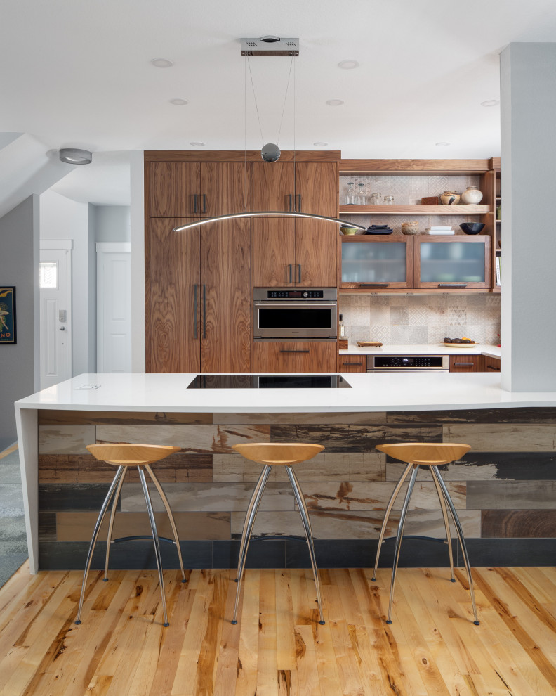 This is an example of a mid-sized modern u-shaped open plan kitchen in Other with an undermount sink, flat-panel cabinets, medium wood cabinets, quartz benchtops, grey splashback, ceramic splashback, stainless steel appliances, medium hardwood floors, a peninsula and white benchtop.