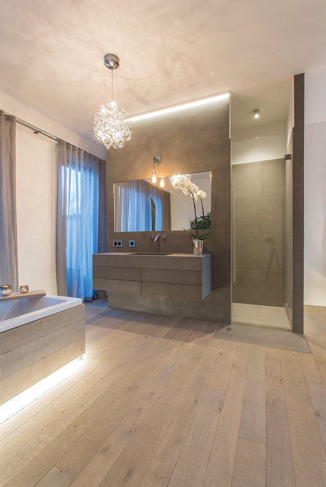 This is an example of a bathroom in Hamburg with flat-panel cabinets, grey cabinets, a drop-in tub, a curbless shower, grey walls, light hardwood floors, a console sink, concrete benchtops, beige floor and an open shower.