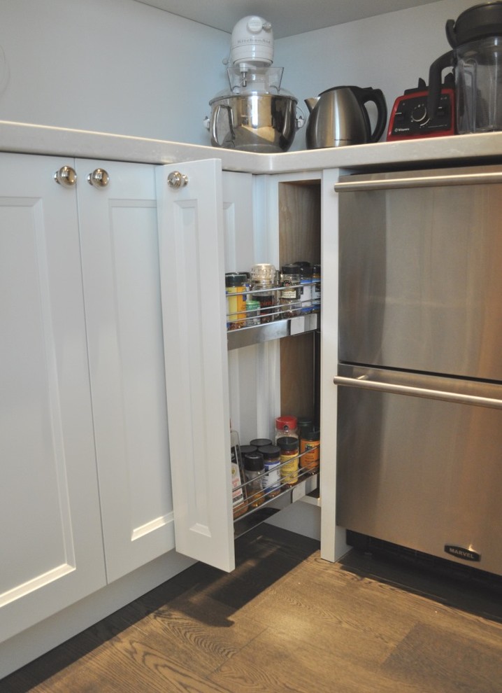 This is an example of a transitional u-shaped kitchen pantry in Vancouver with shaker cabinets, white cabinets, quartz benchtops, white splashback, ceramic splashback, stainless steel appliances and dark hardwood floors.