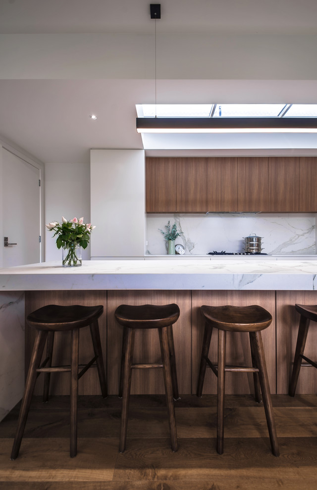 Photo of a mid-sized contemporary galley open plan kitchen in Melbourne with an undermount sink, flat-panel cabinets, white cabinets, marble benchtops, white splashback, stone slab splashback, stainless steel appliances, medium hardwood floors, with island, brown floor and white benchtop.