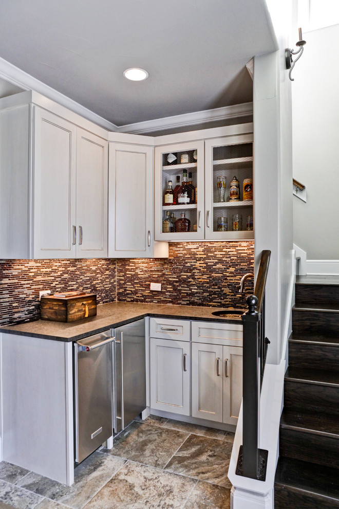 This is an example of a small transitional l-shaped wet bar in Austin with white cabinets, an undermount sink, recessed-panel cabinets, quartz benchtops, multi-coloured splashback, matchstick tile splashback, porcelain floors and brown floor.