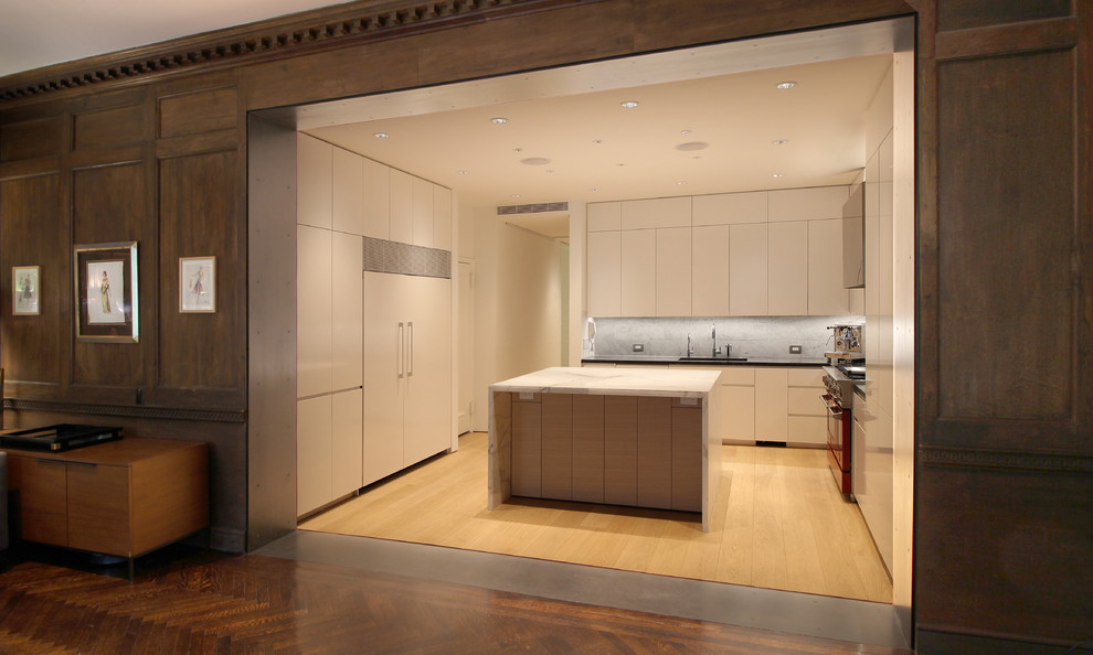 This is an example of a mid-sized modern l-shaped kitchen in New York with an undermount sink, flat-panel cabinets, white cabinets, marble benchtops, grey splashback, stone tile splashback, stainless steel appliances, light hardwood floors, with island, beige floor and black benchtop.