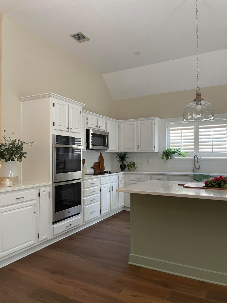 Example of a l-shaped kitchen design with a single-bowl sink, white cabinets, white backsplash, subway tile backsplash, white countertops, quartz countertops, stainless steel appliances and an island