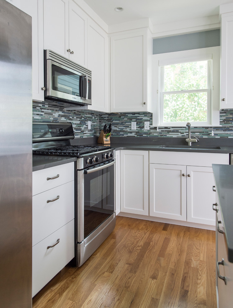 Inspiration for a mid-sized transitional l-shaped medium tone wood floor eat-in kitchen remodel in Boston with shaker cabinets, white cabinets, quartz countertops, gray backsplash, glass sheet backsplash, stainless steel appliances, an island and a single-bowl sink