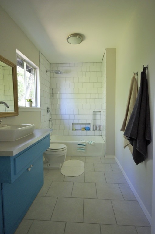 Photo of a mid-sized midcentury kids bathroom in Austin with a vessel sink, furniture-like cabinets, blue cabinets, laminate benchtops, a drop-in tub, an open shower, a two-piece toilet, white tile, ceramic tile, grey walls and porcelain floors.