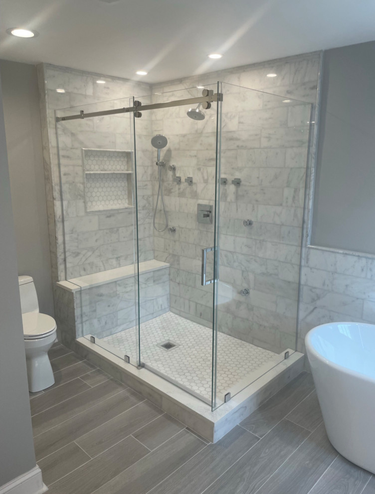 Photo of a large modern master bathroom in New York with flat-panel cabinets, white cabinets, a freestanding tub, a corner shower, a one-piece toilet, gray tile, marble, grey walls, ceramic floors, quartzite benchtops, grey floor, a sliding shower screen, white benchtops, a shower seat and a double vanity.