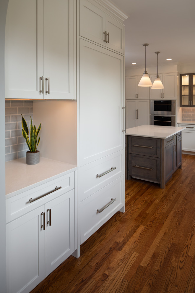 Inspiration for a mid-sized transitional l-shaped medium tone wood floor and brown floor enclosed kitchen remodel with an undermount sink, shaker cabinets, white cabinets, quartz countertops, blue backsplash, subway tile backsplash, stainless steel appliances, an island and white countertops