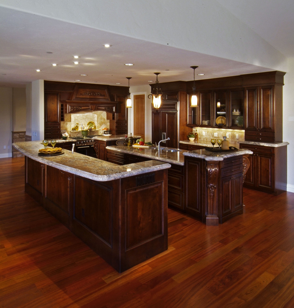 Inspiration for a traditional l-shaped open plan kitchen in Denver with raised-panel cabinets, dark wood cabinets, granite benchtops, beige splashback, stainless steel appliances, medium hardwood floors and multiple islands.