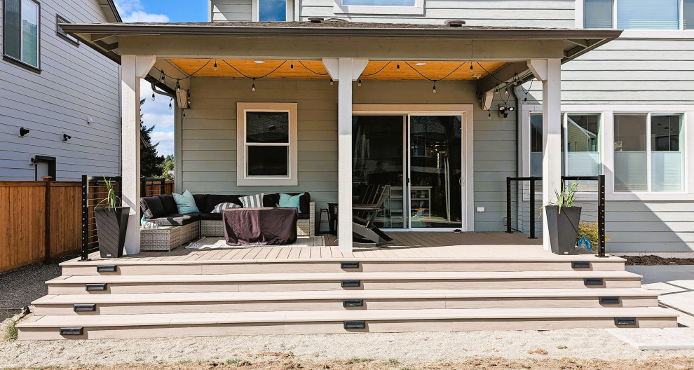 This is an example of a mid-sized arts and crafts backyard and ground level deck in Seattle with an awning and cable railing.