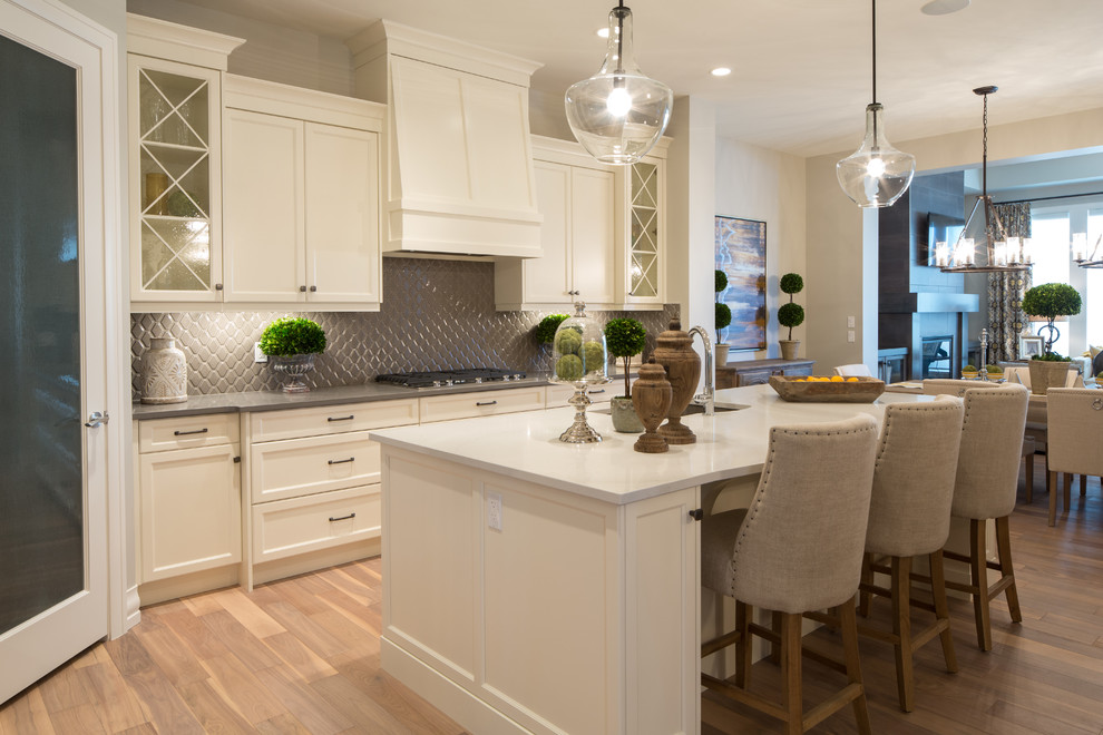 Inspiration for a large transitional l-shaped eat-in kitchen in Calgary with an undermount sink, shaker cabinets, white cabinets, quartzite benchtops, grey splashback, ceramic splashback, stainless steel appliances, light hardwood floors and with island.