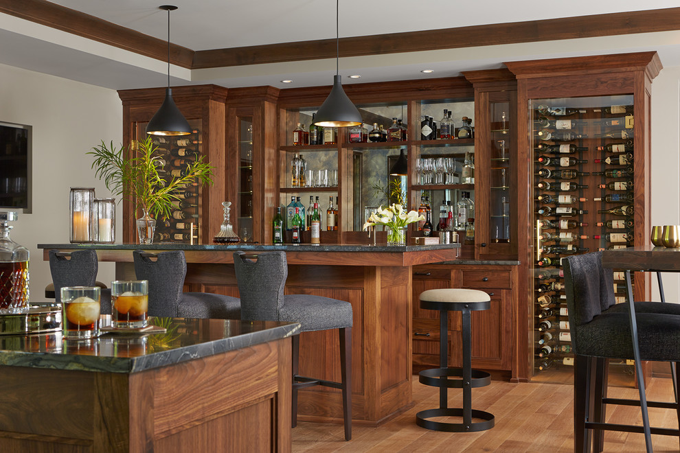 Photo of an expansive eclectic home bar in Minneapolis with recessed-panel cabinets, dark wood cabinets, granite benchtops, medium hardwood floors and brown floor.