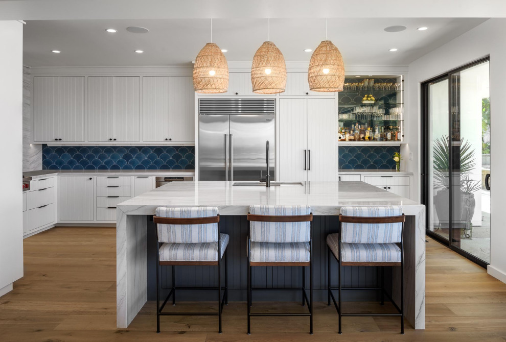 Photo of a beach style u-shaped eat-in kitchen in Santa Barbara with an undermount sink, white cabinets, marble benchtops, blue splashback, stainless steel appliances, medium hardwood floors, with island, brown floor and multi-coloured benchtop.