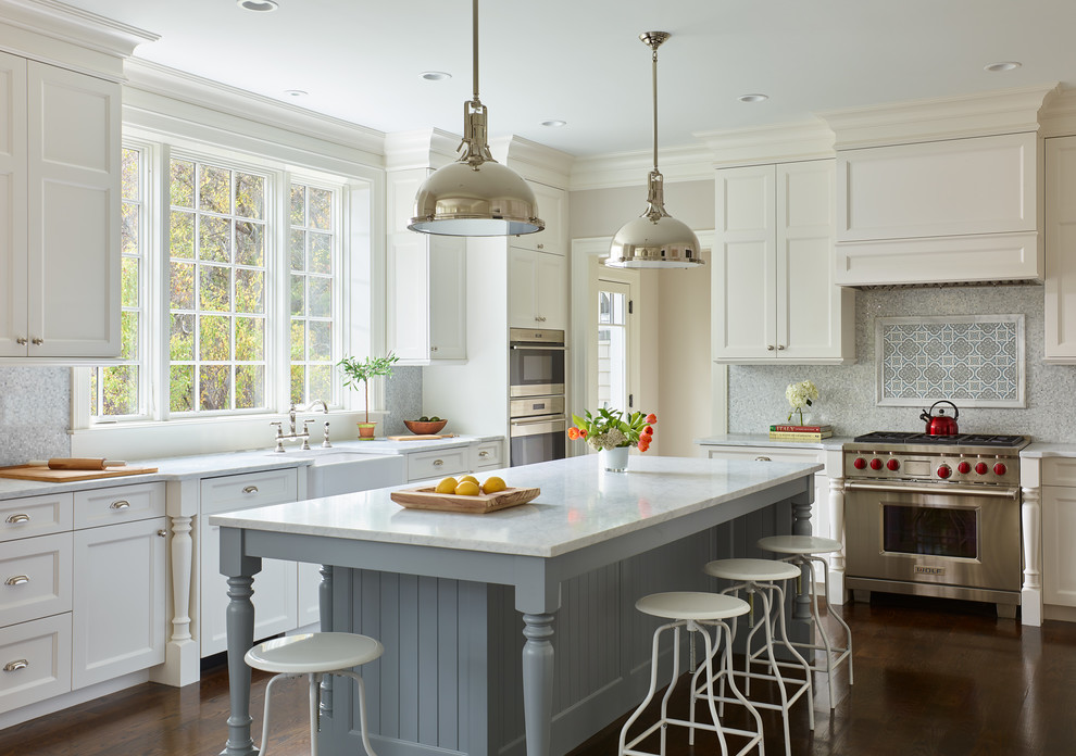 Large transitional l-shaped eat-in kitchen in Boston with a farmhouse sink, beaded inset cabinets, white cabinets, marble benchtops, multi-coloured splashback, mosaic tile splashback, panelled appliances, dark hardwood floors, with island and brown floor.