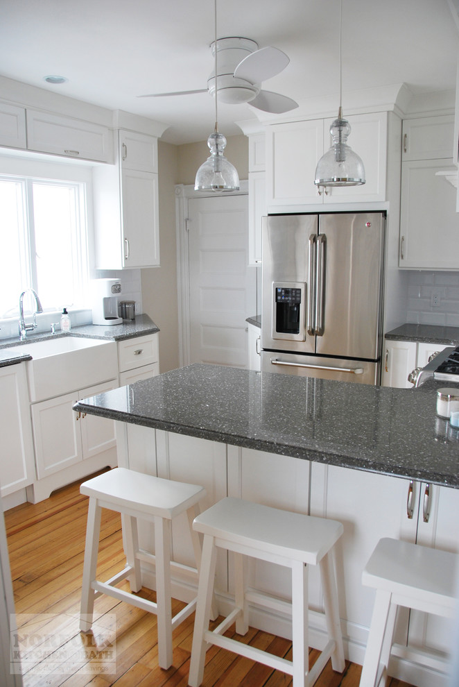 Eat-in kitchen - small transitional u-shaped light wood floor eat-in kitchen idea in Boston with a farmhouse sink, recessed-panel cabinets, white cabinets, quartz countertops, white backsplash, subway tile backsplash, stainless steel appliances and a peninsula