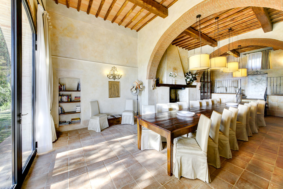 Photo of a large country separate dining room in Florence with beige walls, terra-cotta floors, a standard fireplace and brown floor.